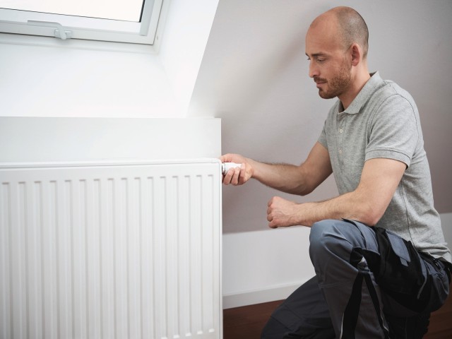 El hombre ajusta el termostato del radiador a la temperatura máxima de la  habitación.